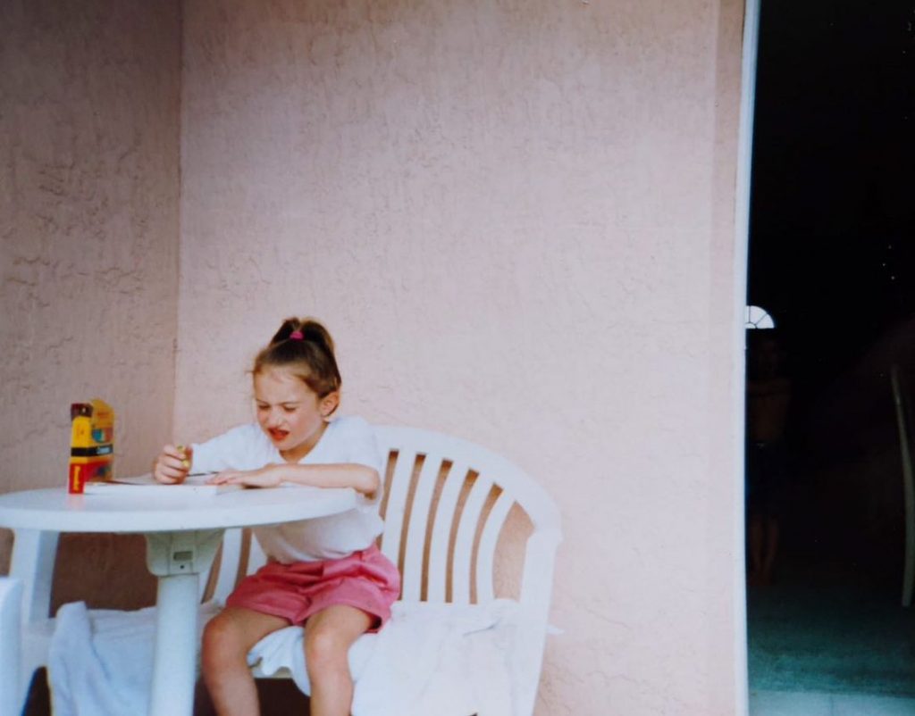 Photo of Kimberley as a child sitting at a table and drawing 